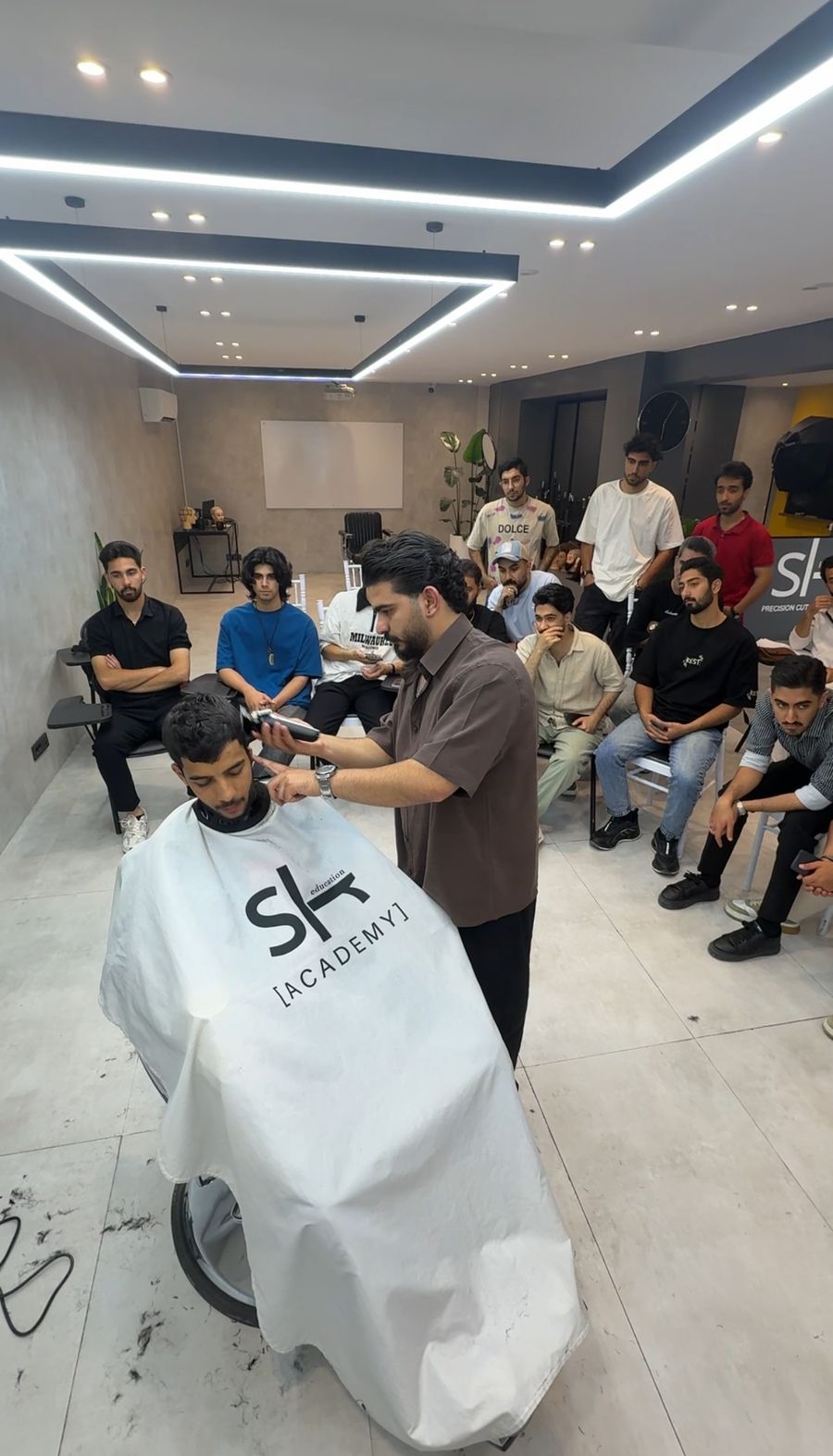 مدرس آکادمی SLR در حال کوتاهی موی مدل با پیشبند SLR Academy مقابل هنرجویان