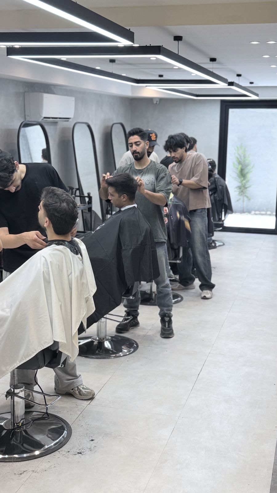 هنرجویان در حال تمرین کوتاهی مو روی مدل در ایستگاه‌های کار آکادمی SLR